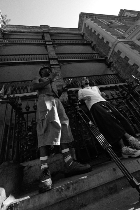 Two men on the steps of a Victorian building, shot from below, in black and white