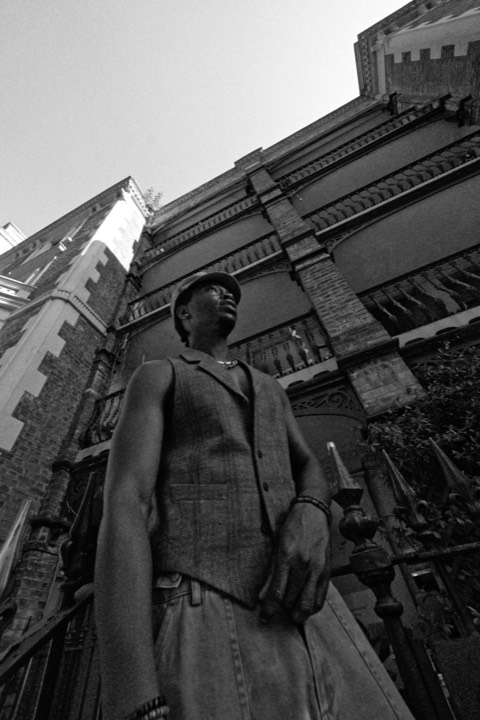 A man in a waistcoat against a brick facade, in black and white