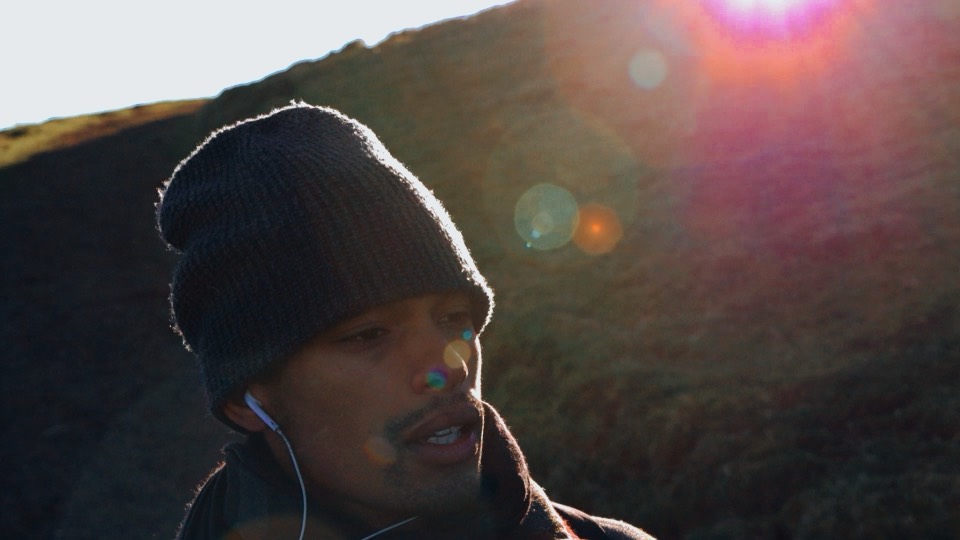 Still from Jeza: a man in a beanie squints into the sun.